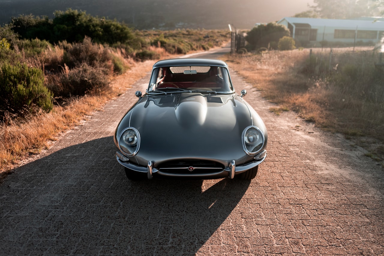 Jaguar E-Type fixed-head coupe in gunmetal grey, photographed head-on on a country road at sunset